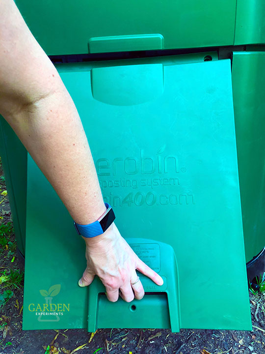 Hand grabbing the door on the composter and opening it up